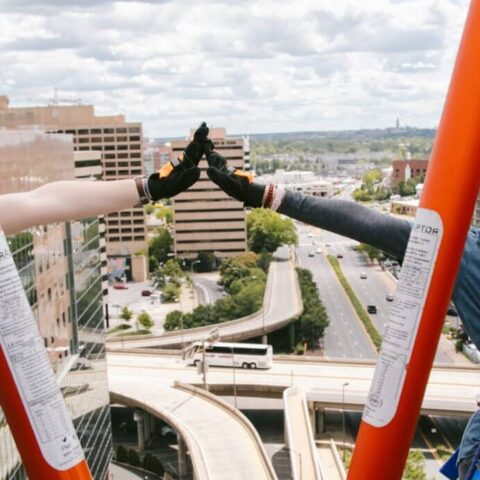 Two women smiling and high-fiving as they rappel down the side of a building.